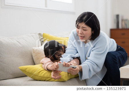 A mother tries to take away her elementary school daughter's smartphone A mother tries to take away her elementary school daughter's smartphone 135123971