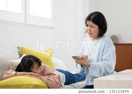 一位母親手裡拿著智慧型手機,訓斥著她的小學生女兒。 一位母親手裡拿著智慧型手機,訓斥著她的小學生女兒。 135123974
