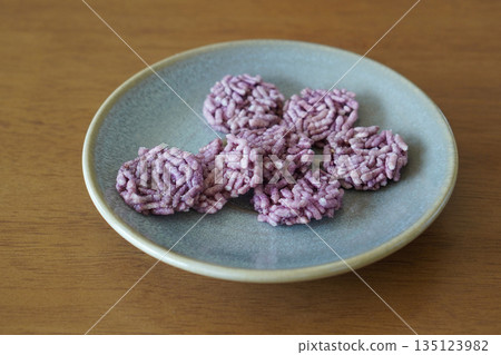 closeup violet seven small pieces of Watermelon Rice Crackers are stacked on top of each other on a blue and green ceramic plate on a wooden table, food, snack, dessert, copy space 135123982