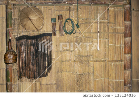 Traditional bamboo wall decorated with indigenous handicrafts, woven hats, and local tools. Authentic ethnic cultural heritage and rustic folk art from Southeast Asia 135124036