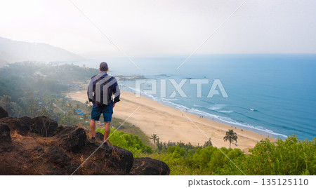 Man with backpack stands on a rock looking at the sea Goa India 135125110