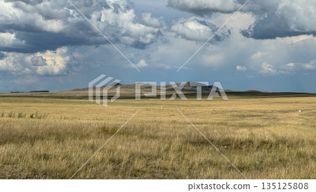 Vast steppe landscape with rolling hills under a dramatic cloudy sky. The clouds leave shadows on the hills. Depicting the beauty and spaciousness of untouched nature. Vast steppe landscape with rolling hills under a dramatic cloudy sky. The clouds leave shadows on the hills. Depicting the beauty and spaciousness of untouched nature. 135125808
