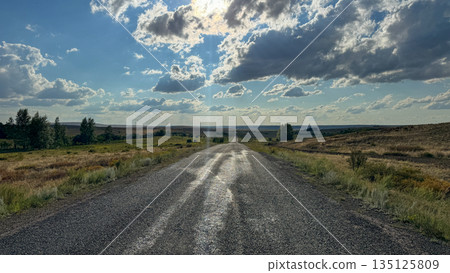 Long old road leading into the distance under a dramatic sky with sun rays breaking through clouds, symbolizing journey and endless possibilities. Long old road leading into the distance under a dramatic sky with sun rays breaking through clouds, symbolizing journey and endless possibilities. 135125809