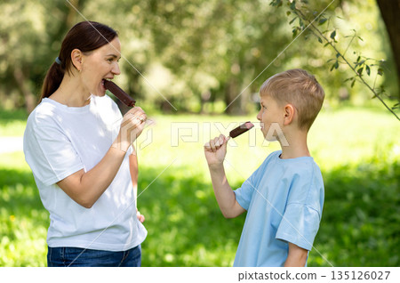 Mother and son eating chocolate ice cream on a stick in summer park Mother and son eating chocolate ice cream on a stick in summer park 135126027