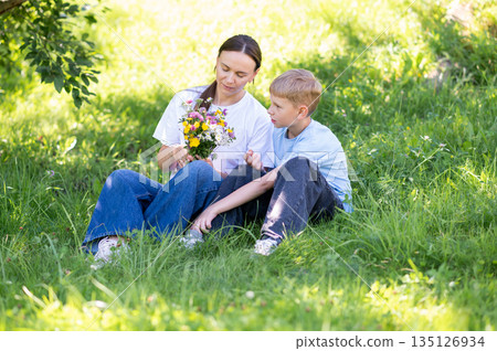 Mother and teen son enjoying time together with wildflowers in summer park Mother and teen son enjoying time together with wildflowers in summer park 135126934