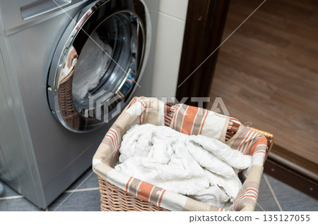 Laundry basket with dirty clothes next to washing machine in bathroom Laundry basket with dirty clothes next to washing machine in bathroom 135127055