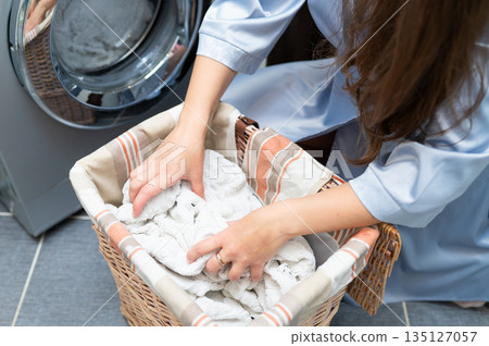 Woman taking dirty laundry from basket to washing machine in bathroom Woman taking dirty laundry from basket to washing machine in bathroom 135127057