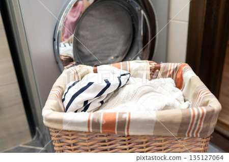 Wicker basket with dirty laundry in front of washing machine 135127064