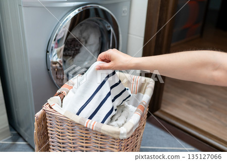 Woman's hand taking clothes from wicker basket to washing machine 135127066