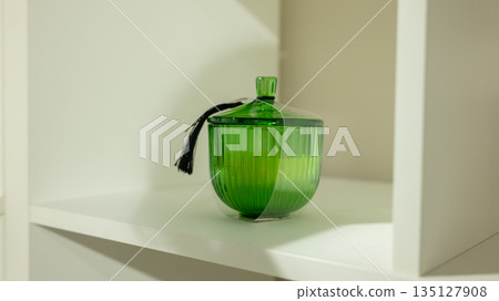 Green glass storage jar with tassel lid on white shelf Green glass storage jar with tassel lid on white shelf 135127908