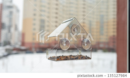 Transparent window bird feeder with suction cups against urban backdrop 135127984