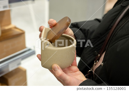 Female shopper examines ceramic container with wooden lid in store Female shopper examines ceramic container with wooden lid in store 135128001