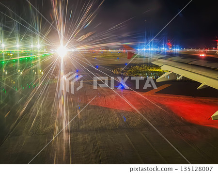 Night airport . An illuminated airport runway at night is captured from an airplane window with vivid starburst light trails and visible aircraft wing. Air travel, night aviation, runway lighting Night airport . An illuminated airport runway at night is captured from an airplane window with vivid starburst light trails and visible aircraft wing. Air travel, night aviation, runway lighting 135128007