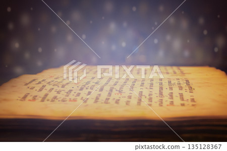 Ancient manuscript glowing under soft magical light with floating particles 135128367