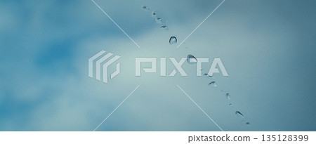 Water droplets on glass surface with soft blue blurred background and smooth gradient tones. Minimal abstract texture with moisture drops creating calm, clean and fresh atmosphere.  135128399