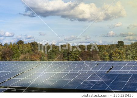 Large solar panel array generating clean renewable energy outdoors with trees and blue sky in background. Sustainable power production concept with copy space Large solar panel array generating clean renewable energy outdoors with trees and blue sky in background. Sustainable power production concept with copy space 135128433