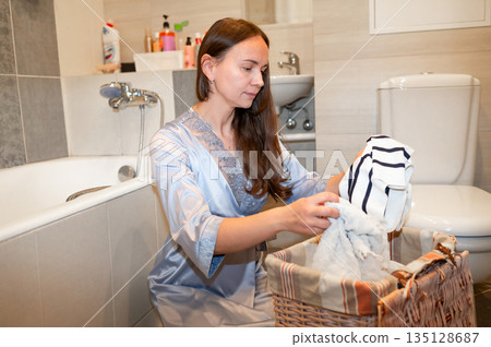 Elegant housewife in silk robe organizing dirty clothes in bathroom, preparing for laundry, concept of home chores and domestic lifestyle Elegant housewife in silk robe organizing dirty clothes in bathroom, preparing for laundry, concept of home chores and domestic lifestyle 135128687