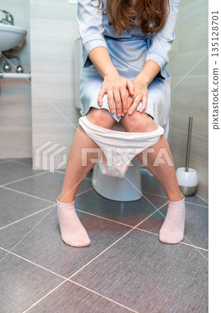 Woman sitting on toilet, experiencing urinary or digestive discomfort 135128701