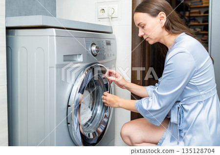 Beautiful housewife closing washing machine, preparing to do laundry at home Beautiful housewife closing washing machine, preparing to do laundry at home 135128704