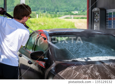 Man washing car with high pressure water at self service car wash station on sunny day 135129132