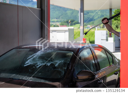 Man washing car with high pressure water at self service car wash station on sunny day 135129134