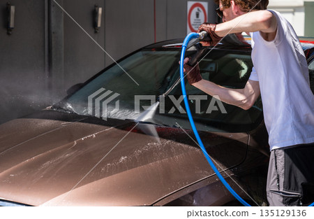 Man washing car with high pressure water at self service car wash station on sunny day Man washing car with high pressure water at self service car wash station on sunny day 135129136