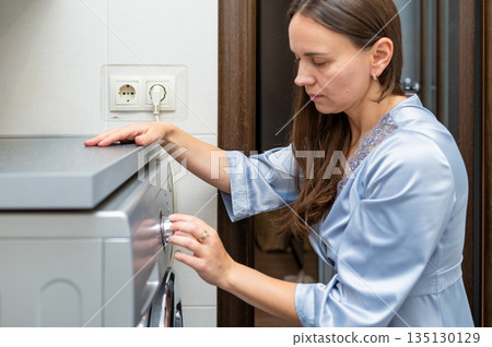 Woman turning on washing machine at home, starting laundry 135130129