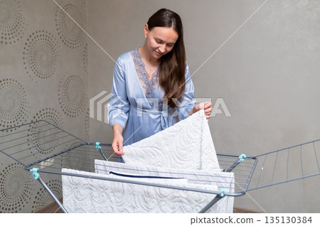 Housewife in silk robe with loose hair hanging freshly washed laundry on drying rack Housewife in silk robe with loose hair hanging freshly washed laundry on drying rack 135130384