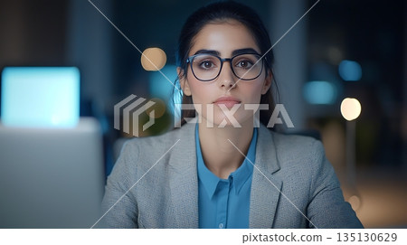 Young Professional Woman in Glasses Focused on Work at Modern Office Desk in Evening Light Young Professional Woman in Glasses Focused on Work at Modern Office Desk in Evening Light 135130629