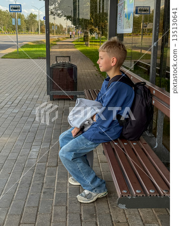 Blonde teenage boy sitting at bus stop waiting for bus 135130641