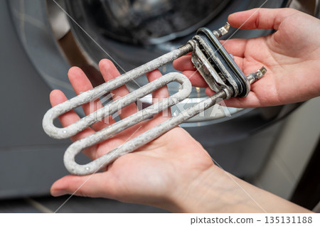 Hands holding washing machine heating element covered with limescale during appliance repair 135131188