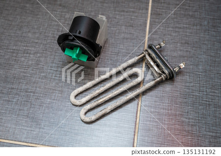 Heating element and pump motor from a washing machine placed on tiled floor after removal 135131192