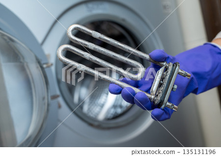 Person in gloves showing removed washing machine heating element covered with limescale 135131196