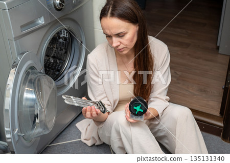 Woman examining washing machine parts heating element and pump motor during home appliance repair Woman examining washing machine parts heating element and pump motor during home appliance repair 135131340