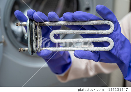 Person in gloves showing removed washing machine heating element covered with limescale Person in gloves showing removed washing machine heating element covered with limescale 135131347