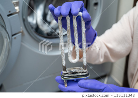 Person in gloves showing removed washing machine heating element covered with limescale Person in gloves showing removed washing machine heating element covered with limescale 135131348