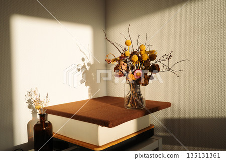 Vases with dried flower bouquets in direct morning sunlight on a table. Everyday home interior scene showing natural light and simple decoration. Concept of home, lifestyle, decor, interior, minimal. 135131361