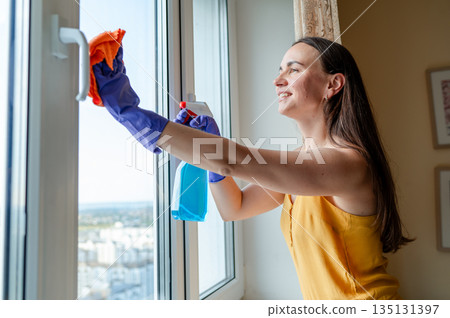 Smiling woman cleaning window on a sunny day Smiling woman cleaning window on a sunny day 135131397