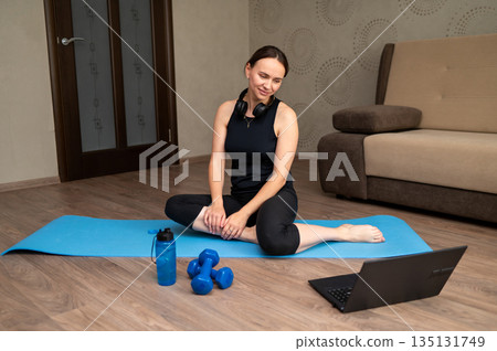 Woman preparing for pilates training at home on yoga mat with laptop 135131749