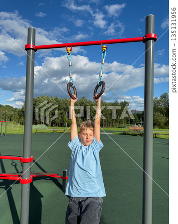Teenage boy training on gymnastic rings at outdoor sports playground on a sunny summer day 135131956
