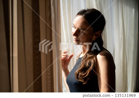 Thoughtful woman looking out the window in sunlight, cozy interior Thoughtful woman looking out the window in sunlight, cozy interior 135131969