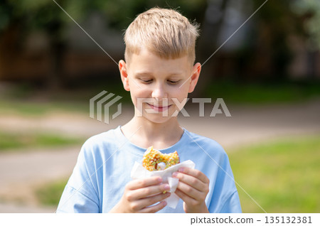 Happy teenage boy eating donut outdoors on a sunny day Happy teenage boy eating donut outdoors on a sunny day 135132381
