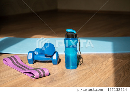 Dumbbells resistance band and water bottle on yoga mat at home 135132514