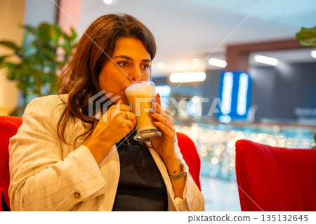 Woman enjoying coffee while sitting in cafe during shopping break. Everyday leisure moment, relaxation pause and modern urban lifestyle in real life commercial environment 135132645
