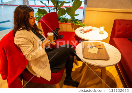 Woman enjoying coffee while sitting in cafe during shopping break. Everyday leisure moment, relaxation pause and modern urban lifestyle in real life commercial environment 135132653