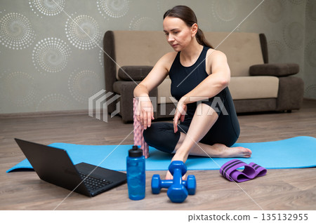 Woman exercising on yoga mat at home following online workout on laptop 135132955