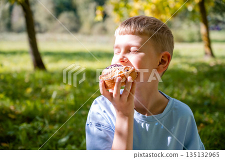 teenage boy eating a cinnamon roll on a picnic on the grass teenage boy eating a cinnamon roll on a picnic on the grass 135132965