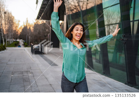 Young woman celebrating success in the city with arms raised 135133526