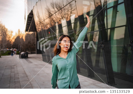 Excited businesswoman waving and laughing near an office building Excited businesswoman waving and laughing near an office building 135133529
