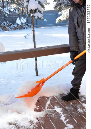 Removing a lot of snow by orange plastic shovel from wooden terrace Removing a lot of snow by orange plastic shovel from wooden terrace 135133762